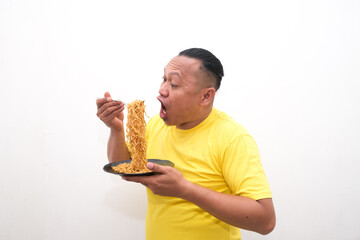 A portrait of a happy Asian man wearing a yellow shirt while eating noodles. Isolated with a white background