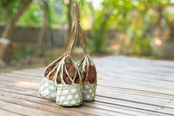 Rectangular objects are wrapped in white paper and then tied with bamboo strips. They are resting on a wooden surface, possibly a boardwalk. The objects appear to be a traditional Thai snack or treat.