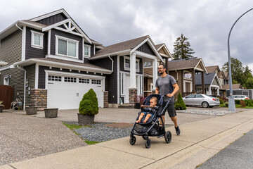 Father Enjoys a Stroll with His Baby in a Stroller Through a Beautiful Suburban Neighborhood in...