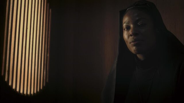 Tilt up shot of African American religious sister sitting in confessional during service in Catholic church