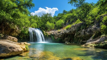 Fototapeta premium The gentle waterfall flows into a clear turquoise pool surrounded by lush green trees and large rocks under a bright, open sky