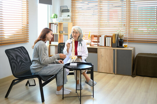 Senior female doctor pointing at vertebrae model while discussing spinal anatomy or treatment options with patient