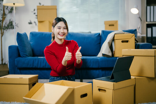 Young woman is smiling and giving thumbs up while unpacking boxes in her new apartment. She is happy with the service provided by the moving company