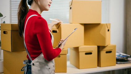 Asian woman carefully checks packages in a warehouse, ensuring accurate delivery. She uses a...
