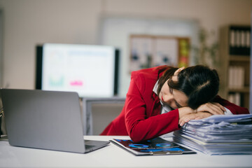 Young businesswoman in a red suit is sleeping on a stack of paperwork at her desk, exhausted after long working hours