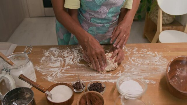 Midsection shot of unrecognizable mom standing behind child and helping her to knead chocolate dough with hands, cooking homemade pastry together in kitchen
