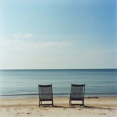 A pair of chairs on the beach, with the calm sea and sky stretching out ahead.