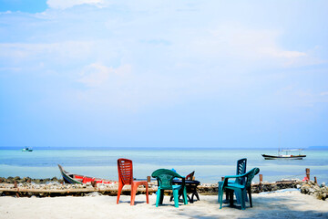 Several plastic chairs with different colors and shapes are on the sand on the beach