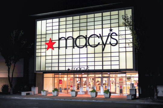 Nighttime exterior of Macy&rsquo;s department store with illuminated signage and visible storefront display, illustrating national retail presence and commercial shopping center architecture