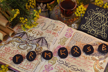 Mystic still life with open book of spells, runes and witchy ritual objects on old altar table. Occult, esoteric, wicca, Halloween and gothic concept. No foreign language, all symbols are fictional