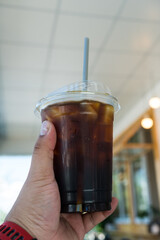 Someone hand holding a plastic cup of iced Americano at coffee shop