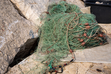 A green nylon fishing net with a floating line attached to small plastic floats is laid out to dry. Seen in Fažana, a coastal town in Croatia that has always lived from the sea and fishing