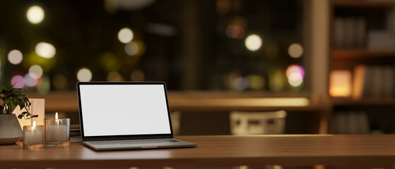 A close-up of a laptop mockup on a wooden table in a minimalist coffee shop at night.