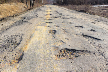 Bad road, cracked asphalt with potholes and big holes. Potholes on the road with stones on the asphalt. The asphalt surface is destroyed on the road. Bad condition of the road, needs repair.