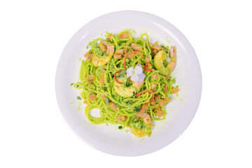 A plate of green spaghetti with shrimp, vegetables, and a creamy avocado sauce, garnished with a flower and chili peppers.