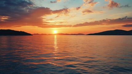 Obraz premium Stunning sunset over calm waters with silhouetted hills on the horizon during a serene evening