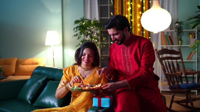 A happy young Indian couple in traditional attire light diyas in their beautifully decorated home filled with flowers and lights,creating cherished moments of joy