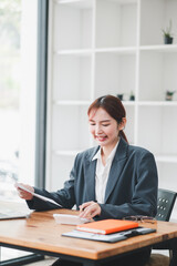 Professional woman in a suit working at a desk in a modern office, reviewing documents and using a laptop.