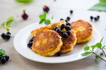 Fried curd cheese pancakes with black currants, on a wooden table