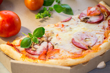 cooked pizza with salami and sausage in a box on a wooden table