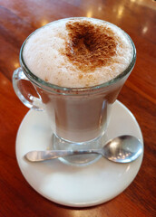 Café capuchino servido en una copa con leche descremada y canela espolvoreada. Fotografía de una bebida caliente tomada con el teléfono celular.