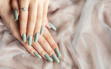 Elegant hands with long green nails resting on soft fabric