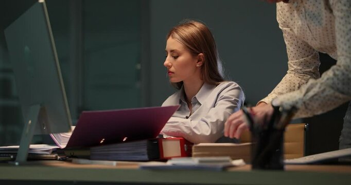 Focused woman checks documents with male assistant staying late in office. Exhausted colleagues keep working on important project at night