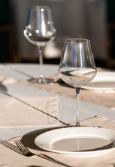 Stylish table setting. Glass glasses, plates, cutlery on the table. Wedding service, reception at the dining table. A birthday, a baptism, a festive event.