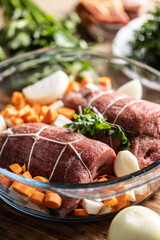 Raw beef tenderloin in a glass baking dish with root vegetables, ready to be processed into the Czech national dish - Sirloin on cream