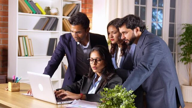 Young Indian manager working in an office, guiding and supporting her subordinates as they collaborate on a project report, in a professional environment