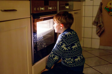 Cute blond boy baking muffins or pie in domestic kitchen. Happy child having fun with helping,...