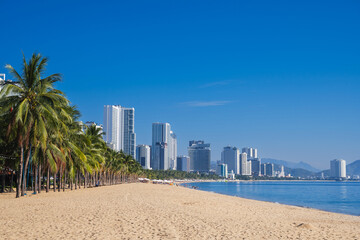 Sandy beach with palm trees by the sea in a resort town with skyscrapers in summer in Nha Trang in Vietnam during the day