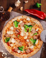 Delicious pizza lying on wooden table surrounded by fresh ingredients
