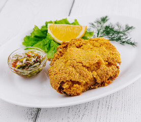 Breaded fish fillet served on white plate with lemon and sauce