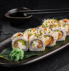 Sushi rolls covered with sesame seeds lying on a black plate on dark stone table
