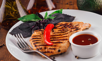 Grilled chicken breast with tomato sauce served on white plate on wooden table
