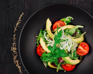 Fresh salad with avocado and tomatoes on black plate