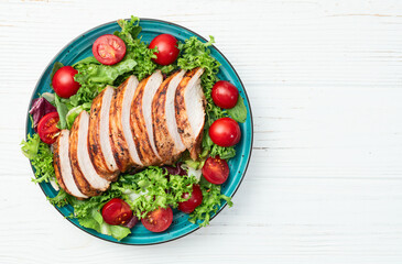 Grilled chicken breast ( fillet ) with lattuce salad and cherry tomatoes . Top view