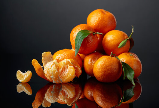 Tangerines or clementines with green leaves on a black background.