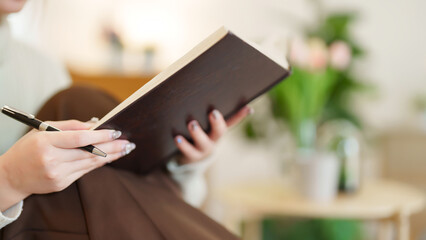 Closeup hands of young asian women holding the book to reading and learning about education while sitting on couch to relaxation and doing activity for spending time with slow life lifestyle at home