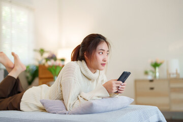 Young asian women in sweater lying on comfortable couch to enjoying with surfing entertainment on smartphone while relaxation and doing activity to spending time with slow life lifestyle at home