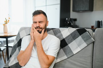 Man with sensitive teeth suffering from pain at home