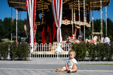 Adorable toddler sitting in front of colorful amusement park carousel