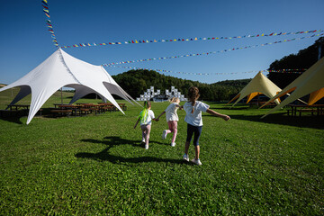 Children playing at outdoor festival with colorful tents under clear skies