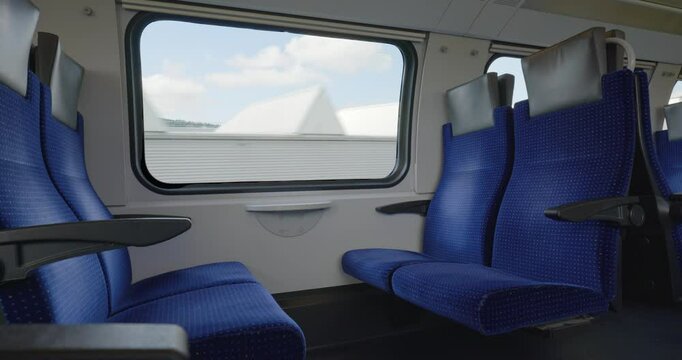 Empty bench seats inside moving public passenger train in Europe. Wide angle view, large windows, green summer nature landscape outside, real time, no people