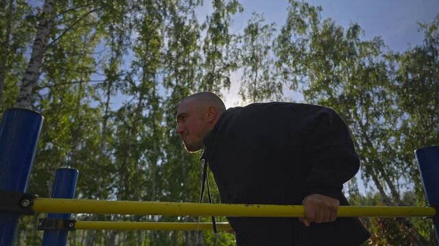 The bald man is training. Man doing triceps dip exercise on parallel bars with extra weights at open gym.