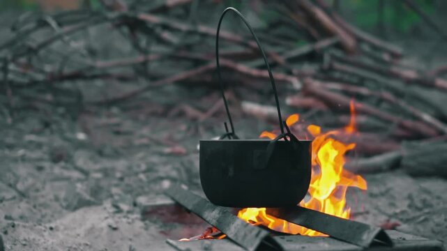 Close-up view of an empty pot hanging over a campfire. Water is poured into the pot and potatoes are added.