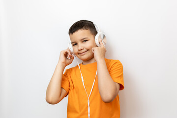 A boy in an orange T-shirt listens to music with white headphones with pleasure.