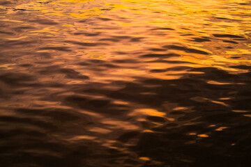 Golden reflections on rippling water create a mesmerizing texture with warm hues and dynamic...