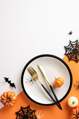 Elegant Halloween vertical themed table setting with pumpkins, spiders, and bats on an orange and white background